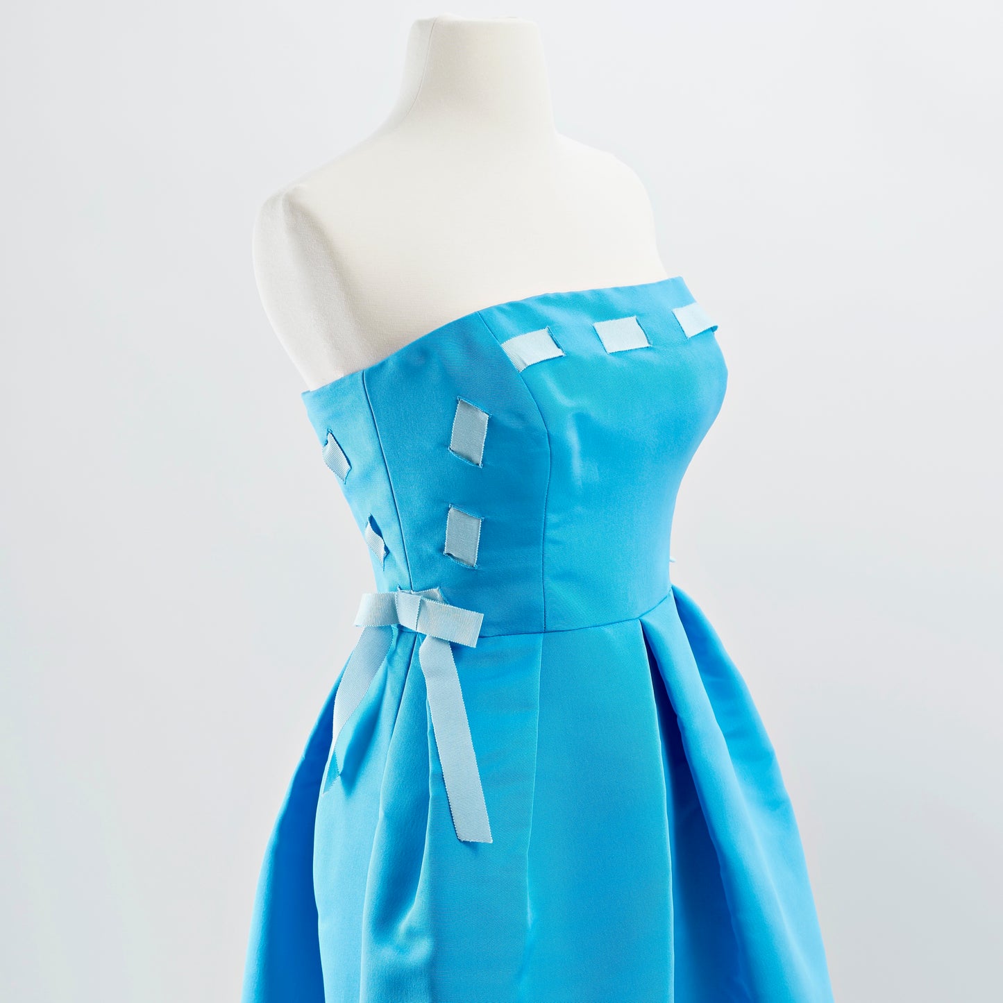 Detail shot of bodice of blue strapless silk faille cocktail dress with full skirt and light blue woven ribbon detail and bows at waist